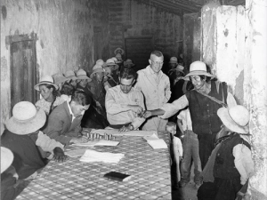 black and white image of the anthropologists Allen Holmberg speaking with indigenous people in Vicos, Peru. Sitting at a table.